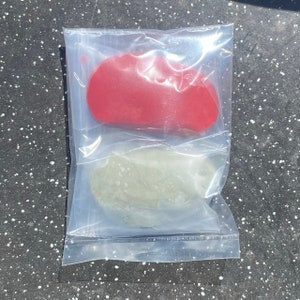 May include: Two small, flat, irregularly shaped pieces of clay in a clear plastic bag. One piece is red and the other is green.