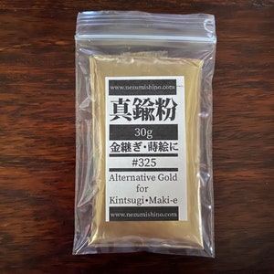 May include: A small resealable bag containing a gold powder labeled "真鍮粉" (Shin'chū-fun) or "Brass Powder" in Japanese. The bag also includes the text "30g", "金継ぎ・蒔絵に" (Kintsugi Maki-e), "#325", "Alternative Gold for Kintsugi Maki-e", and "www.nezumishino.com".