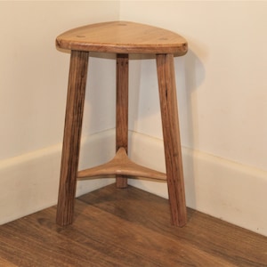 May include: A triangular wooden stool with three legs and a natural wood finish.