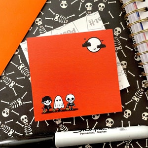May include: Red card with a black and white illustration of three trick-or-treaters. A ghost, a skeleton, and a boy with a pumpkin bucket. The card has a black moon and clouds in the upper right corner.