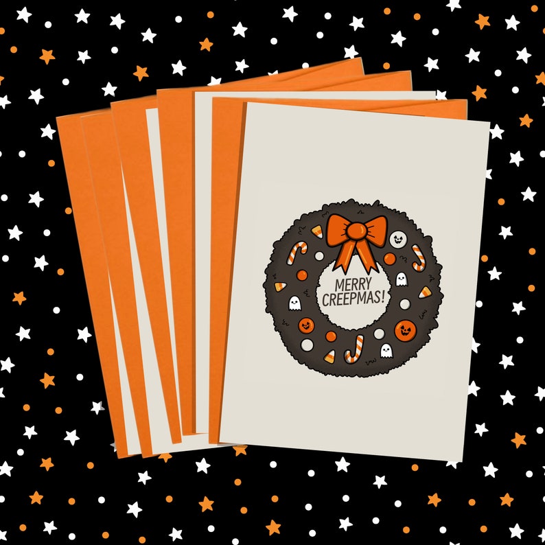 Puede incluir: Un conjunto de tarjetas de felicitaci&oacute;n de Halloween. Las tarjetas presentan un dise&ntilde;o de corona con caramelos, fantasmas y el texto "MERRY CREEPMAS!". Los sobres son naranjas con rayas blancas.