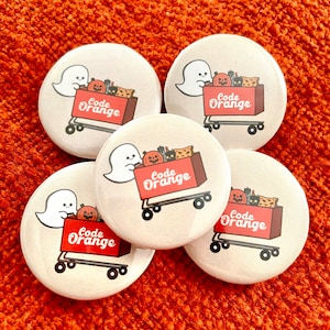 May include: Five round white buttons with a ghost pushing a red shopping cart filled with Halloween decorations. The cart has the text "Code Orange" on the side.