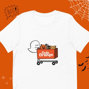 Może przedstawiać: Biała koszulka z kreskówkowym duchem pchającym czerwony wózek zakupowy wypełniony artykułami na Halloween. Wózek ma napis "Code Orange" pomarańczowym tekstem.
