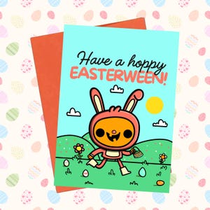 May include: A greeting card featuring a cartoon bunny in a pink suit, holding a basket of eggs, and the text "Have a hoppy EASTERWEEN!". The card has a light blue background with a green field and a yellow sun. An orange envelope is behind the card.