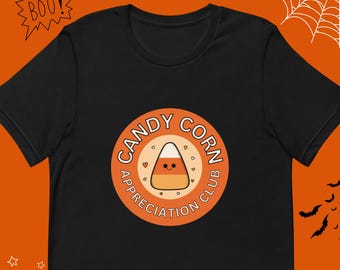 Puede incluir: Camiseta negra con un gráfico circular naranja que dice "Candy Corn Appreciation Club" con un maíz dulce de dibujos animados en su interior.