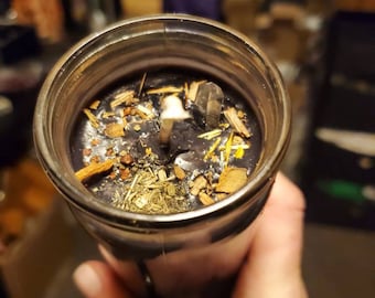 May include: A black candle with herbs and crystals embedded in the wax. The candle is in a glass jar.
