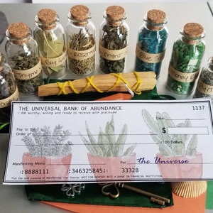 May include: A set of small glass bottles with cork tops filled with dried herbs and crystals. The bottles are labeled with the names of the herbs and crystals, including Basil, Bay Leaf, Rosemary, Thyme, Mint, Blue Salt, Money Bag, and Pyrite. The bottles are arranged in a row on a table, along with a wooden stick and a check printed with "The Universal Bank of Abundance".