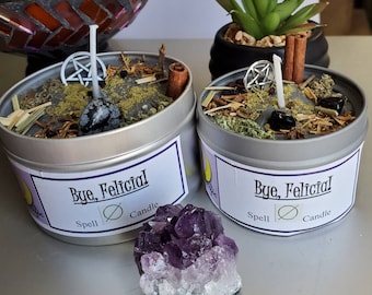 May include: Two silver candle tins with black lids and gray wax. The candles are labeled "Bye, Felicital Spell Candle".  A purple amethyst crystal sits in front of the candles.