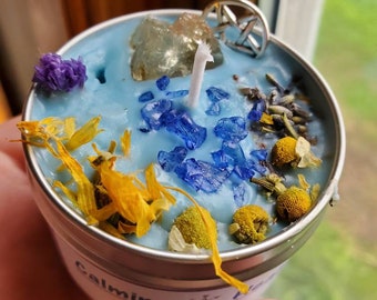 May include: A blue calming spell candle with dried flowers, blue glass shards, and a clear crystal. The candle is in a metal tin with the words "Calming Spell Candle" on the label.