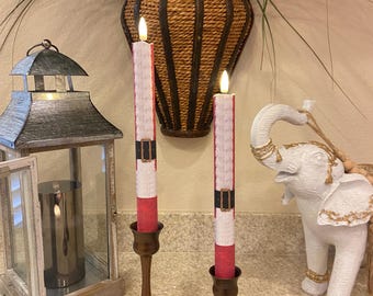 May include: Two battery-operated, Santa-themed candles with a remote control. The candles are red, white, and black, and sit in bronze-colored candle holders. A white elephant statue and a decorative lantern are also in the image.