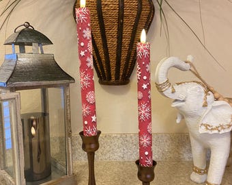 May include: Two red and white snowflake-patterned candles in bronze candle holders. A remote control sits in front of the candles. A decorative lantern and a white elephant statue are also in the image.