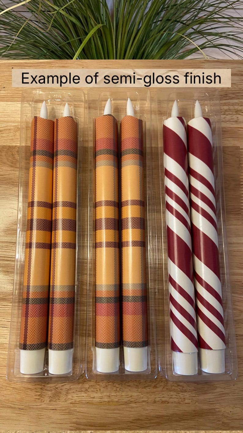 May include: Candles in clear plastic packaging. Two sets of candles are visible. One set has an orange plaid pattern, and the other has red and white stripes. The text "Example of semi-gloss finish" is above the candles.