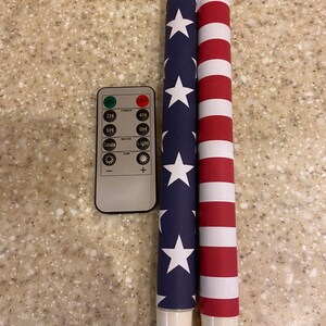May include: Two decorative pillar candles with patriotic designs. One candle has a blue background with white stars, the other red and white stripes. A remote control with timer and light settings is also included.