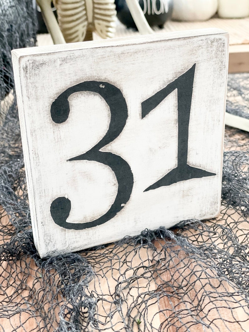 May include: White wooden sign with black painted numbers "31" on it. The sign is sitting on a black mesh fabric.
