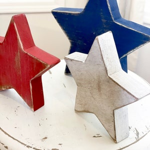 Puede incluir: Tres estrellas de madera en rojo, blanco y azul, sentadas sobre una base circular blanca y desgastada.