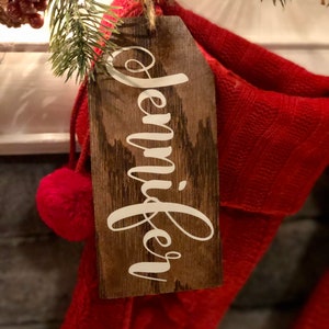 May include: A wooden Christmas stocking tag with the name "Jennifer" written in white paint.
