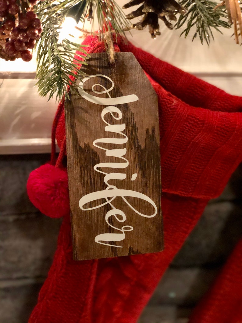 May include: A wooden Christmas stocking tag with the name "Jennifer" written in white paint.