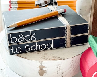 May include: Two black painted wooden boxes stacked on top of each other. The top box says "back" and the bottom box says "to school". A yellow pencil is laying on top of the boxes.