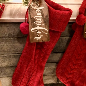 May include: Red knitted Christmas stocking with a wooden tag that says "Jennifer" hanging from it.