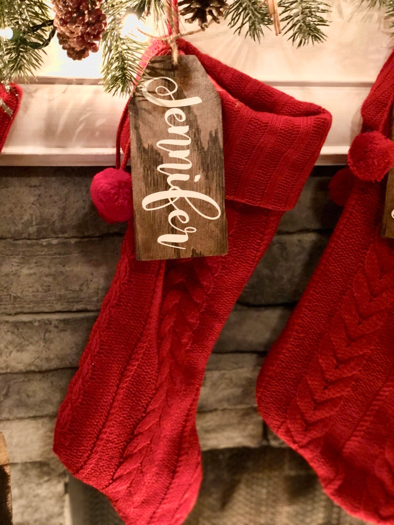 May include: Red knitted Christmas stocking with a wooden tag that says "Jennifer" hanging from it.