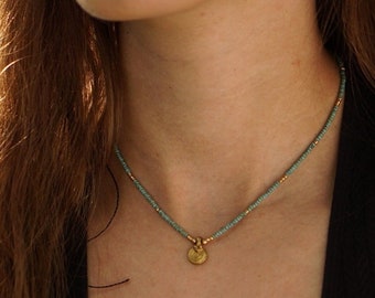May include: A delicate gold necklace with a small round pendant. The necklace is made of tiny turquoise and gold beads.