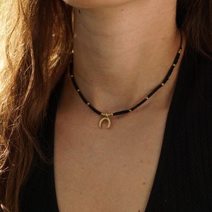 Peut inclure: Un collier ras de cou noir avec un pendentif en forme de croissant de lune doré.