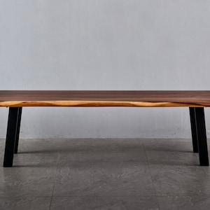 May include: A long wooden bench with a natural edge top and black metal legs. The bench is made of dark wood with a light brown grain.