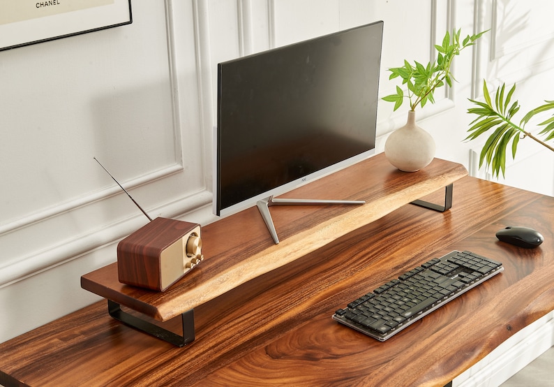 May include: A wooden desk with a monitor stand, a keyboard, a mouse, and a vintage radio. The monitor stand is made of a single piece of wood with a natural edge. The desk is made of dark wood with a natural grain.