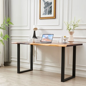 Pode incluir: Uma escrivaninha de madeira com tampo de borda viva e pernas de metal preto. Um laptop, uma l&acirc;mpada, uma x&iacute;cara e um vaso com flores est&atilde;o sobre a escrivaninha.