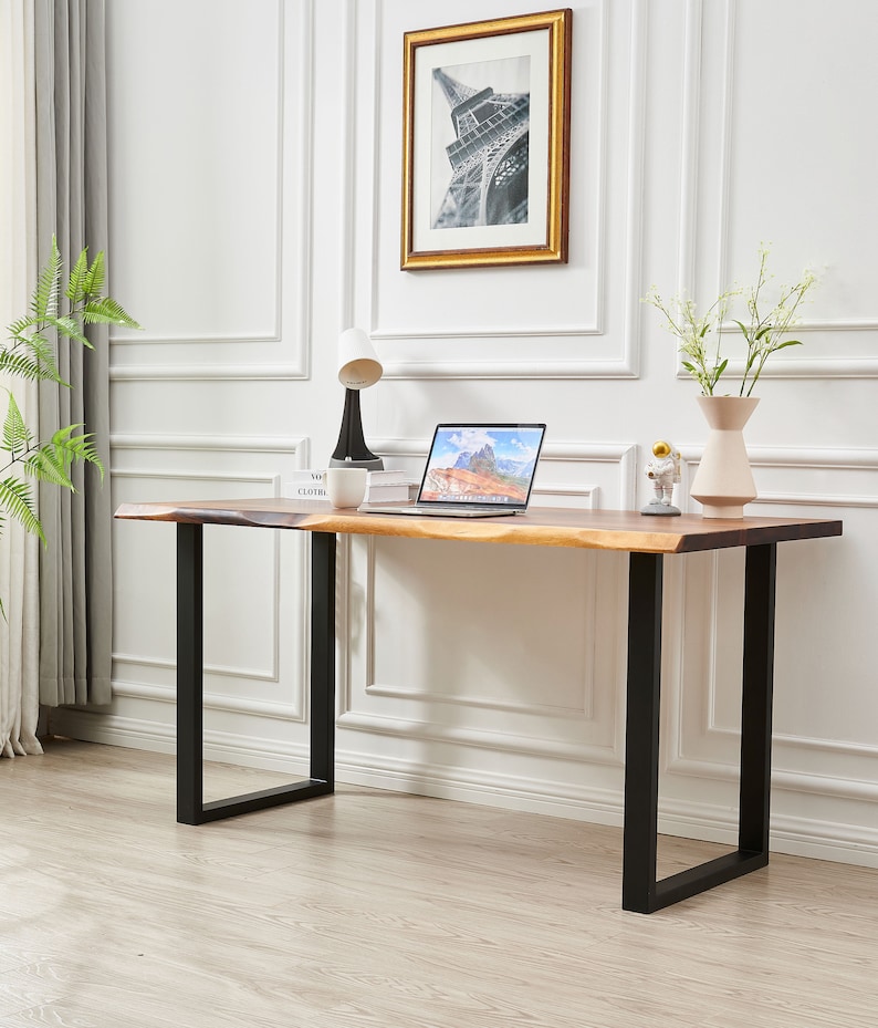 Pode incluir: Uma escrivaninha de madeira com tampo de borda viva e pernas de metal preto. Um laptop, uma l&acirc;mpada, uma x&iacute;cara e um vaso com flores est&atilde;o sobre a escrivaninha.