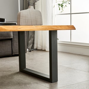 May include: A wooden coffee table with a live edge top and black metal legs. The table is in a living room setting with a vase of dried flowers on top.