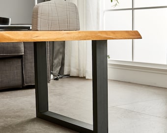 May include: A wooden coffee table with a live edge top and black metal legs. The table is in a living room setting with a vase of dried flowers on top.