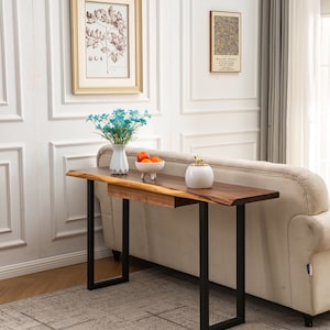May include: A wooden console table with a live edge top and black metal legs. The table has a drawer and is sitting on a patterned rug in front of a white sofa.