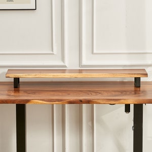 May include: A wooden standing desk with a black metal frame and a smaller wooden shelf attached to the top. The desk has a natural wood finish.