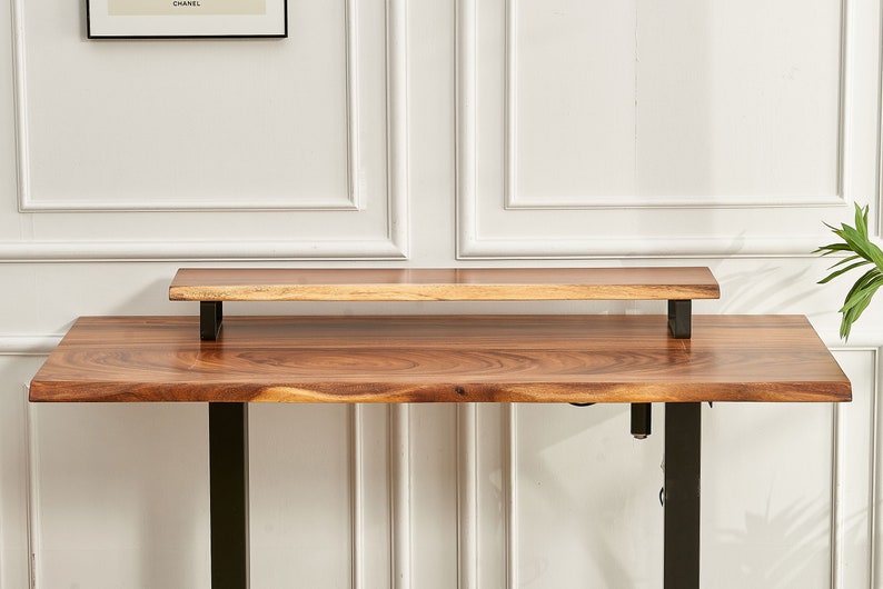 May include: A wooden standing desk with a black metal frame and a smaller wooden shelf attached to the top. The desk has a natural wood finish.