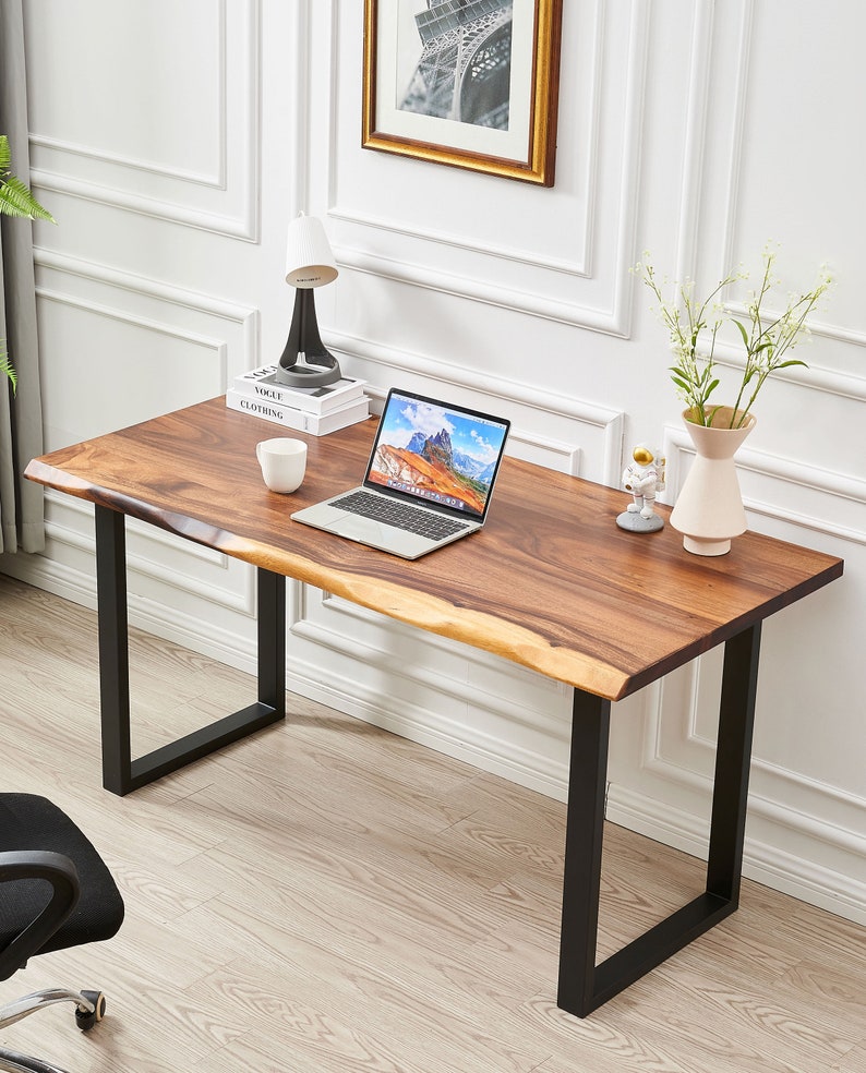 Pode incluir: Uma escrivaninha de madeira com tampo de borda viva e pernas de metal preto. Um laptop, uma x&iacute;cara, uma l&acirc;mpada e um vaso com flores est&atilde;o sobre a escrivaninha.