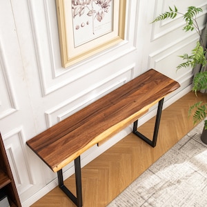 May include: A wooden console table with a live edge top and black metal legs. The table is sitting on a wood floor with a white rug.