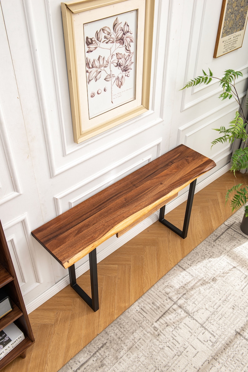 May include: A wooden console table with a live edge top and black metal legs. The table is sitting on a wood floor with a white rug.