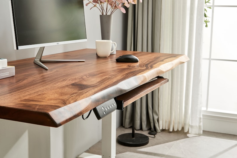 May include: A wooden standing desk with a live edge top and a pull-out keyboard tray. The desk has a white base and a black control panel for adjusting the height.