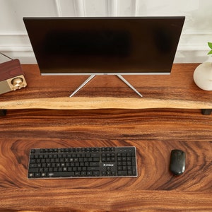 May include: A wooden desk with a black keyboard, a computer mouse, and a monitor on a wooden stand. The desk has a natural wood grain pattern.