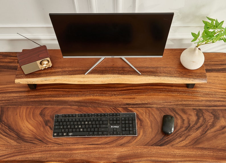 May include: A wooden desk with a black keyboard, a computer mouse, and a monitor on a wooden stand. The desk has a natural wood grain pattern.
