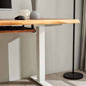 May include: White standing desk with a wooden top and a keyboard tray. The desk has a white base with a rectangular foot.