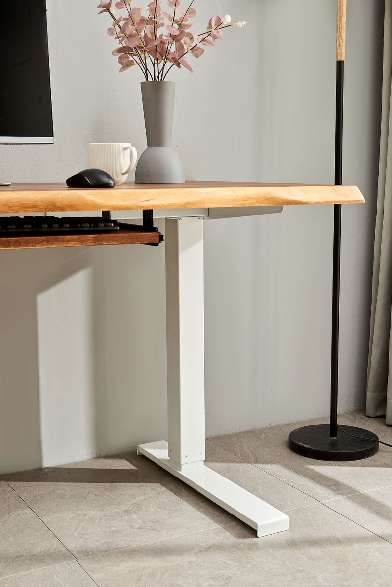 May include: White standing desk with a wooden top and a keyboard tray. The desk has a white base with a rectangular foot.