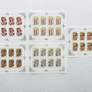 Op de afbeelding: Verschillende vellen vintage postzegels met paddenstoelillustraties. De postzegels tonen verschillende paddenstoelsoorten in tinten rood, bruin, geel en wit. Elke postzegel staat tegen een witte achtergrond met bloemenranden.