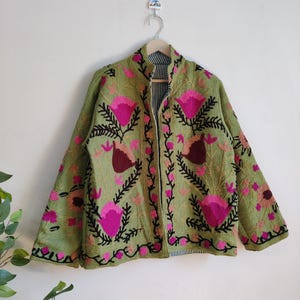 Puede incluir: Una chaqueta verde bordada con dise&ntilde;os florales rosas y negros. La chaqueta tiene un cuello mandar&iacute;n y mangas largas.