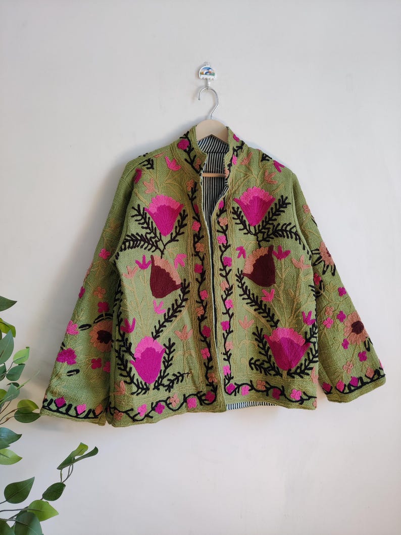 Puede incluir: Una chaqueta verde bordada con dise&ntilde;os florales rosas y negros. La chaqueta tiene un cuello mandar&iacute;n y mangas largas.