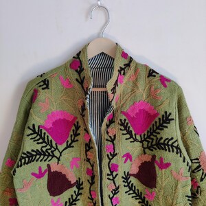 Puede incluir: Una chaqueta verde bordada con dise&ntilde;os florales rosas y marrones. La chaqueta tiene un cuello mandar&iacute;n y una cremallera.