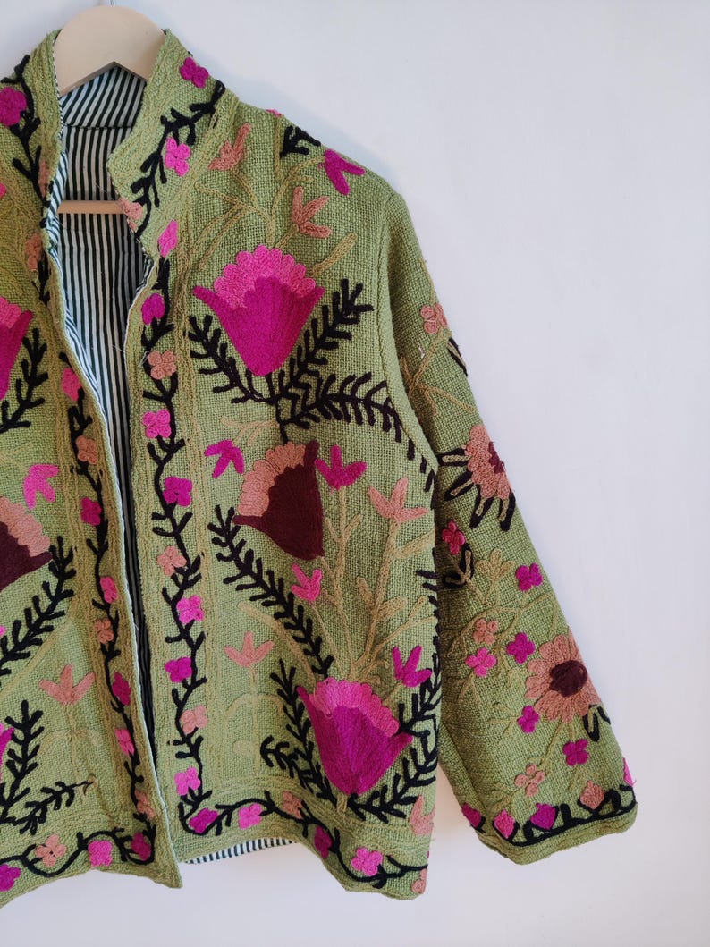 Puede incluir: Una chaqueta verde bordada con dise&ntilde;os florales rosas y marrones. La chaqueta tiene un cuello mandar&iacute;n y un forro a rayas blanco y negro.