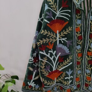 May include: A dark green velvet jacket with colorful floral embroidery. The jacket features orange, red, blue, and purple flowers with white stems and gold accents. The collar and edges are also embroidered with a striped lining.