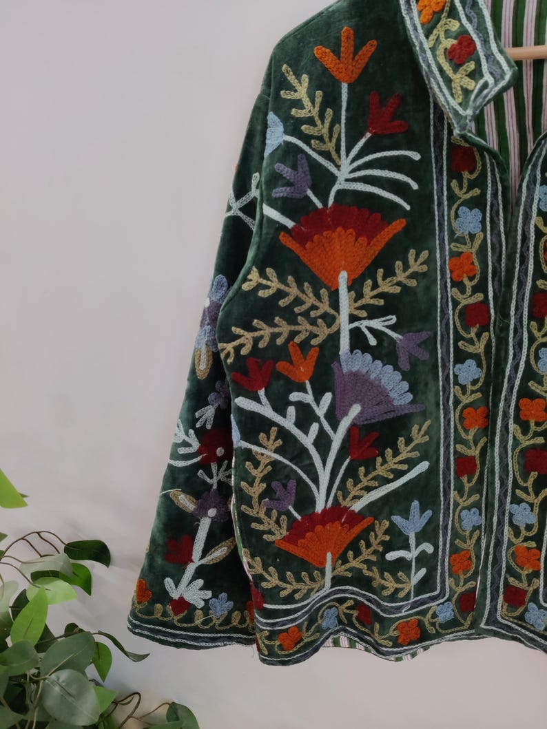 May include: A dark green velvet jacket with colorful floral embroidery. The jacket features orange, red, blue, and purple flowers with white stems and gold accents. The collar and edges are also embroidered with a striped lining.